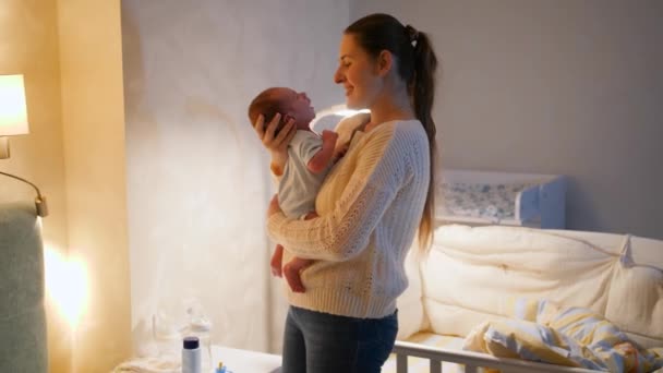 Feliz sorrindo jovem mãe abraçando e segurando seu bebê recém-nascido no quarto à noite. Conceito de recém-nascidos, pais carinhosos e carinhosos e felicidade familiar. — Vídeo de Stock