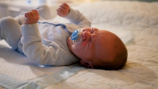 Porträtt av ett litet nyfött barn som suger på strumpor eller napphållare och börjar gråta i spjälsängen på natten. COncept av gråtande barn och sömnlösa nätter — Stockvideo