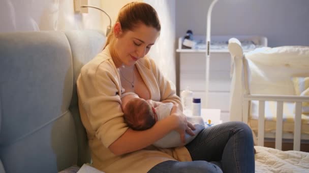 Smiling young mother breastfeeding her newborn baby boy in bed before going to sleep. Concept of healthy and natural baby nutrition. Breastfeeding and parenting — Stock Video