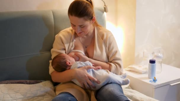 Panning colpo di sorridente giovane donna si svegliò di notte alimentando il suo bambino appena nato con latte materno. Concetto di nutrizione sana e naturale del bambino. Salute della madre e del bambino — Video Stock