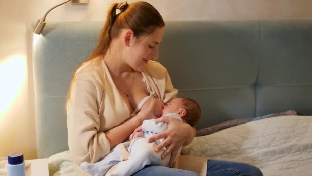 Hermosa madre joven amamantando a su pequeño bebé recién nacido en la cama por la noche. Concepto de nutrición saludable y natural del bebé. Salud de la madre y del niño — Vídeos de Stock