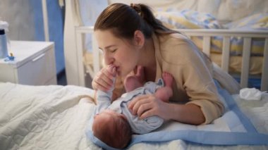 Gülümseyen güzel bir anne masaj yapıyor ve küçük bebeğini gece yatakta yatarken seyrediyor. Mutlu ebeveynlik ve aile mutluluğu