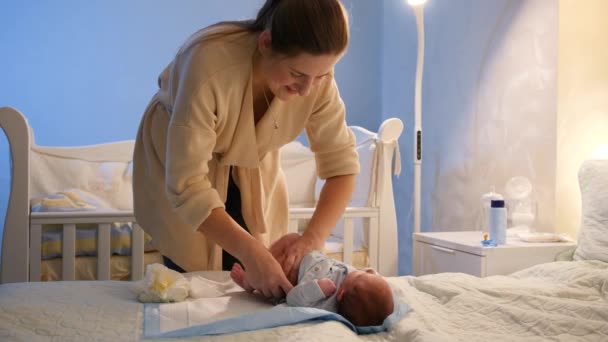 Hermosa mujer sonriente poniéndose pañales en su pequeño bebé acostado en la cuna por la noche. COncept de felicidad familiar e higiene del bebé. — Vídeos de Stock