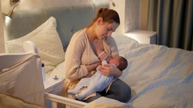 Yorgun anne, yeni doğmuş bebeğini gece yatakta sallayıp besliyor. Sağlıklı ve doğal bebek beslenmesi kavramı. Anne ve çocuğun sağlığı.