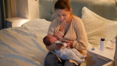 Genç ve güzel bir kadın gece bebeğini emzirirken akıllı telefon kullanıyor. Sağlıklı ve doğal bebek beslenmesi kavramı. Anne ve çocuğun sağlığı.
