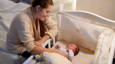 Mutlu gülümseyen anne beşik sallıyor ve yeni doğmuş bebeğini gece yatakta yatarken seyrediyor. Mutlu ebeveynlik ve aile mutluluğu kavramı