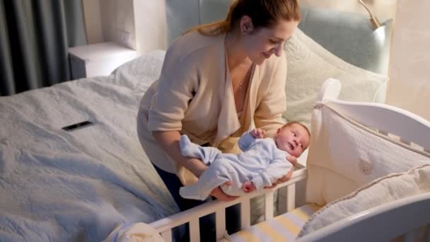 Belle jeune mère attentionnée mettant son nouveau-né dans un berceau et le couvrant d'une couverture chaude la nuit. Concept de parentalité heureuse et de bonheur familial — Video