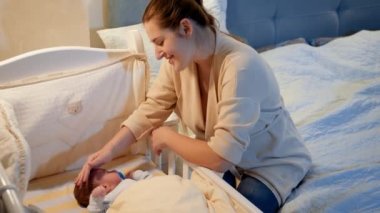 Mutlu gülümseyen anne, uykusuz bir gecede bebeğini beşiğinde yatarken seyredip okşuyor. Mutlu ebeveynlik ve aile mutluluğu kavramı