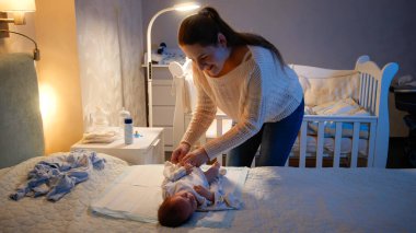 Genç, şefkatli anne gece bebeğini giydiriyor. Ebeveynler yeni doğan çocuğa kıyafet giydiriyorlar. Sevgi ve şefkat kavramı, yeni doğmuş bebekler ve aile mutluluğu..