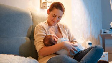 Güzel, genç bir anne yeni doğmuş bebeğini gece yatakta emziriyor. Sağlıklı ve doğal bebek beslenmesi kavramı. Anne ve çocuğun sağlığı