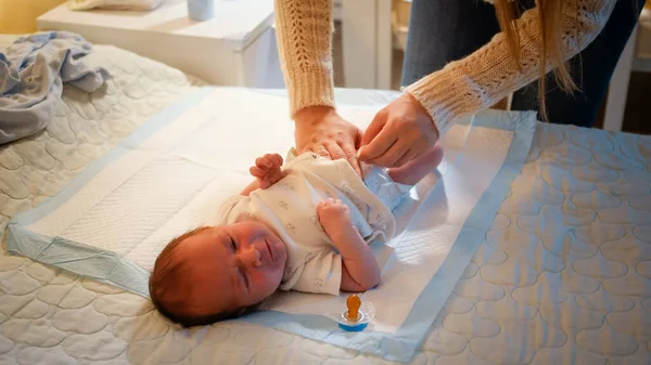 Madre joven cambiando pañales desordenados a su bebé recién nacido llorando en la cama por la noche. Concepto de higiene del bebé, padres cariñosos y cariñosos y felicidad familiar. — Foto de Stock