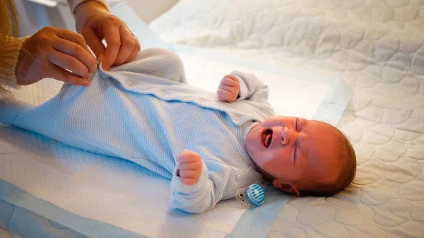 Bebé recém-nascido se vestindo e chupando chupeta na cama à noite. mãe carinhosa mudando de roupa de seu filho bebê. Conceito de recém-nascidos, pais amorosos e carinhosos e felicidade familiar — Fotografia de Stock