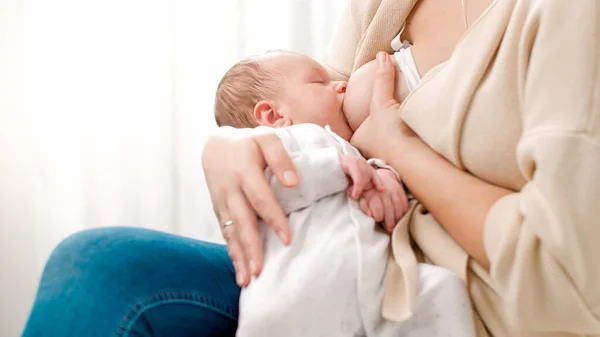 Young caring mother sitting on bed and feeding her newborn baby boy with breast milk. Concept of healthy and natural baby breastfeeding nutrition. — Stock Photo, Image