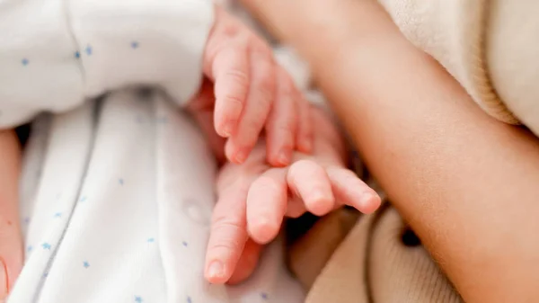 Primer plano de las pequeñas manos del bebé recién nacido mientras duerme en la joven madre cariñosa — Foto de Stock