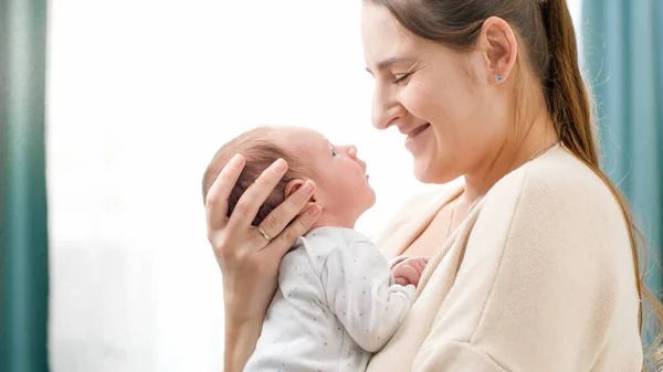 Portrét dvoutýdenního chlapečka s mladou starostlivou matkou proti velkému oknu v domě. Koncept rodinného štěstí a milujících rodičů s malými dětmi — Stock fotografie