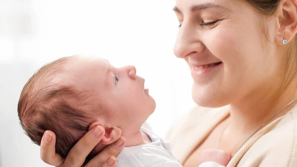 Szoros portré mosolygó anyáról, imádnivaló újszülött babával a nagy, fényes ablakkal szemben. A családi boldogság fogalma és a kisgyermekes szerető szülők — Stock Fotó