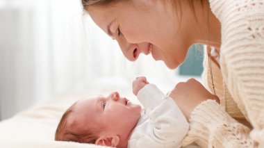 Sevgi dolu bir annenin gülümseyen portresi ve güneşli bir günde yeni doğmuş bebeğini yatakta yatarken izlemek. Aile mutluluğu ve küçük çocuklu sevgi dolu ebeveynler.