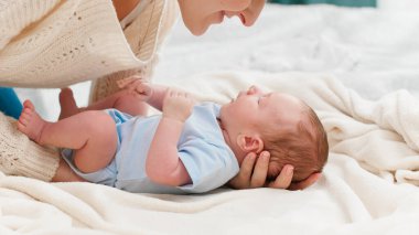 Genç, şefkatli bir anne, küçük oğlunu yatak odasında yumuşak bir battaniyeye sardı. Aile mutluluğu ve küçük çocuklu sevgi dolu ebeveynler..
