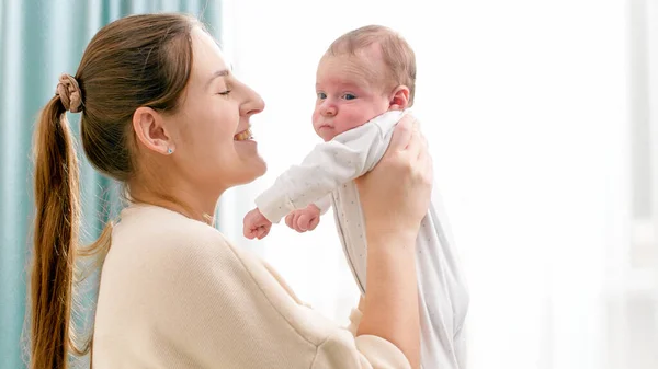 Egy boldog mosolygó anya portréja, ahogy az újszülött kisfiát a nagy ablakhoz szorítja a házban. A családi boldogság fogalma és a kisgyermekes szerető szülők — Stock Fotó