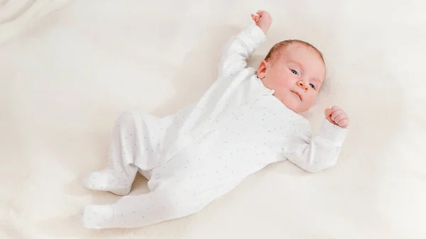 Top view on adorable newborn baby in white bodysuit lying on bed and looking on bright sun. Newborn babies at home — Stock Photo, Image