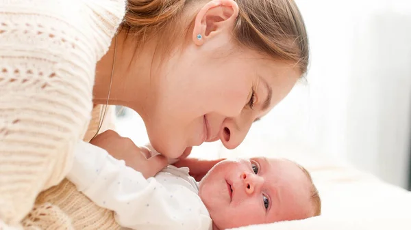 Closeup portrait of smiling young mother looking on her newborn baby son against big window at house — Stock Photo, Image