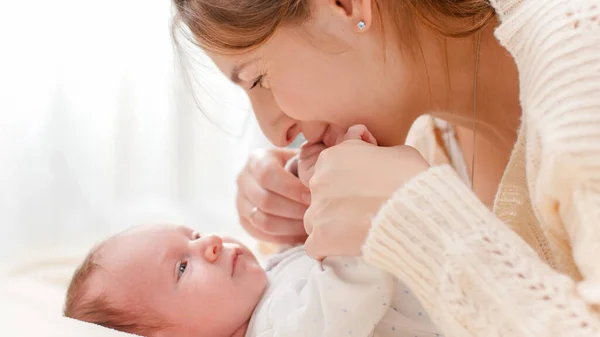 Primo piano ritratto di bella madre sorridente che bacia le sue mani bambine sdraiato sul letto contro una grande finestra in camera da letto — Foto Stock