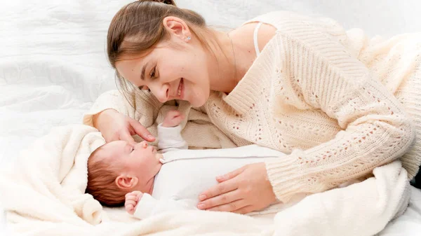 Happy smiling mother playing and tickling her 1 months old newborn baby lying on bed. Concept of family happiness and loving parents with little children — Stock Photo, Image