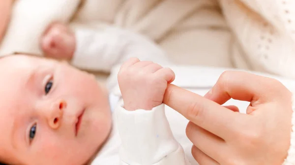 Primo piano del neonato che stringe e cattura il dito delle madri con piccole mani. Concetto di felicità familiare e genitori amorevoli con bambini piccoli — Foto Stock