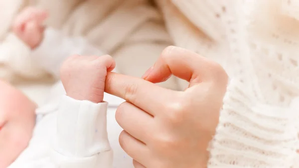 Närbild skott av lilla nyfödda barnet handen håller stora fingret av ung mor — Stockfoto