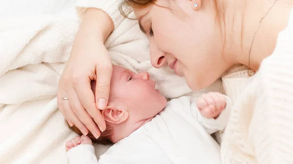 Ujęcie z bliska małego noworodka leżącego obok matki i płaczącego. Szczęśliwa uśmiechnięta kobieta patrząca na swoje dziecko. Pojęcie szczęścia rodzinnego i kochających rodziców z małymi dziećmi — Zdjęcie stockowe