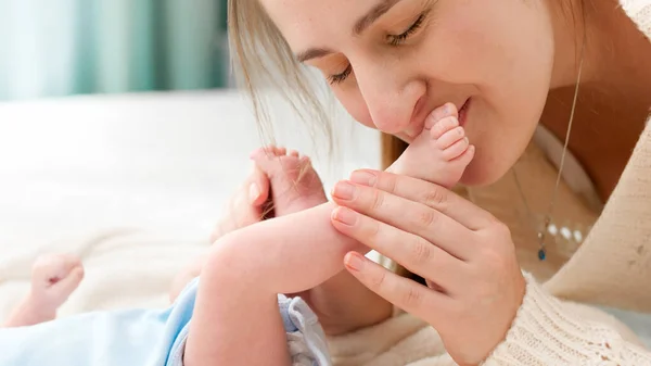 Close-up de jovem mãe deitada na cama e beijando pequenos pés de seu filho recém-nascido — Fotografia de Stock