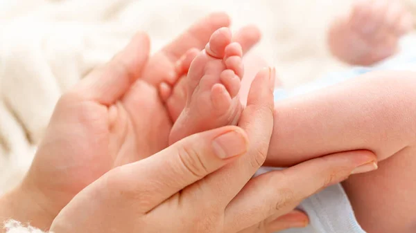 Primer plano de la mujer acariciando suavemente con la mano los pequeños pies de su hijo recién nacido con la piel perfecta. Concepto de felicidad familiar y padres amorosos con niños pequeños — Foto de Stock