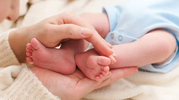 Close-up da mãe segurando pequenos pés de seu bebê recém-nascido deitado na cama — Fotografia de Stock