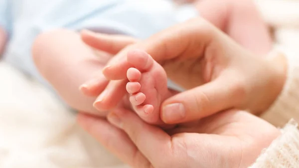 Nahaufnahme einer Mutter, die kleine Füße ihres neugeborenen Jungen massiert, der auf dem Bett liegt — Stockfoto