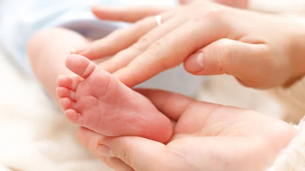 Nahaufnahme einer Mutter, die kleine Füße ihres Neugeborenen berührt und streichelt. Konzept des Familienglücks und liebevoller Eltern mit kleinen Kindern. Babymassage und Gesundheitsfürsorge — Stockfoto