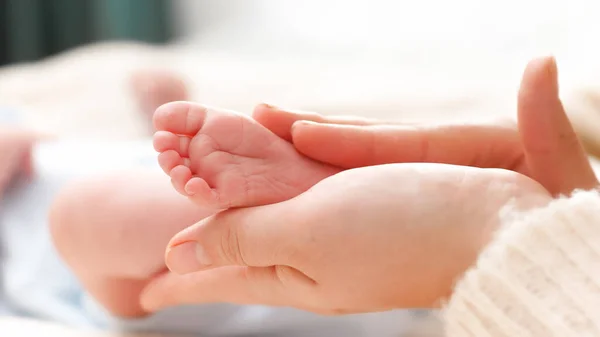 Petits pieds de bébé dans les mains des femmes. Jeune mère touchant doucement et caressant ses jambes de bébé nouveau-né. Concept de bonheur familial et de parents aimants avec de petits enfants. — Photo