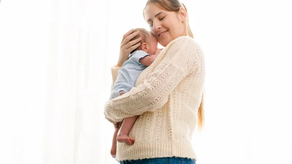 Portret van moeder knuffelende pasgeboren baby in zonlicht schijnt door groot raam in huis — Stockfoto