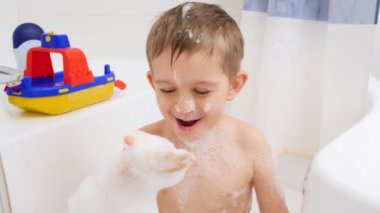 Yavaş çekim gülen çocuğun banyo yapması ve el ele sabun köpüğü üflemesi. Evde çocuk hijyeni ve sağlık hizmetleri kavramı. Çocuklar eğleniyor ve oynuyor.