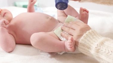 Annesinin talk pudrası sürerken küçük oğlunun kirli bezlerini değiştirdiği fotoğraf. Bebekler, yeni doğan hijyen ve sağlık hizmetleri kavramı. Önemsiz ebeveynler