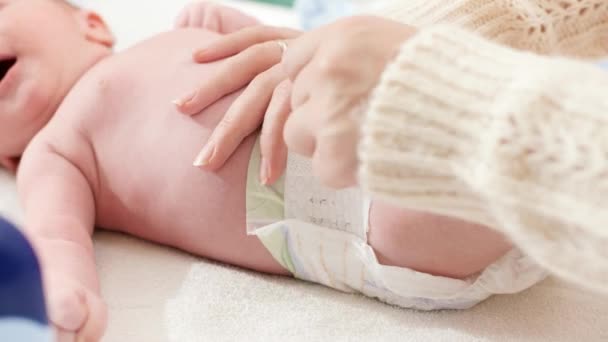 Close-up de jovem mãe carinhosa mudando fralda de seu filho recém-nascido deitado na mesa de vestir no quarto. Conceito de bebês e higiene e cuidados de saúde do recém-nascido. Cuidar dos pais com crianças pequenas. — Vídeo de Stock