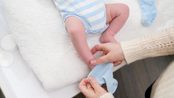 Close-up da mãe vestindo seu filhinho recém-nascido e vestindo meias azuis em pés minúsculos. Conceito de bebês e higiene e cuidados de saúde do recém-nascido. Cuidar dos pais com crianças pequenas. — Vídeo de Stock