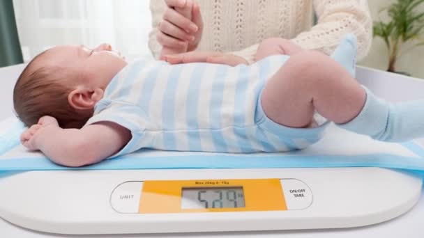 Jeune mère bienveillante caressant son petit fils nouveau-né tout en le pesant sur des balances numériques à l'hôpital. Concept d'hygiène et de santé des bébés et des nouveau-nés. Parents aidants avec de petits enfants. — Video