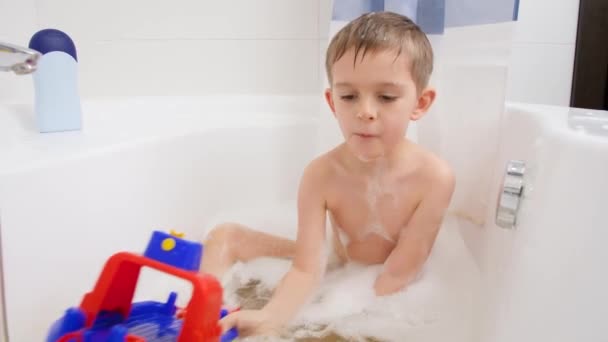 Cute little boy biorąc kąpiel w domu i gry iwth kolorowy statek zabawki lub łodzi. Pojęcie higieny dzieci i opieki zdrowotnej w domu. Dzieci dobrze się bawią i bawią — Wideo stockowe