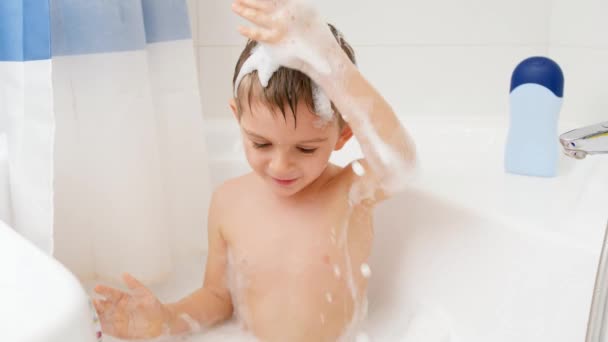 有趣的小男孩在洗澡，把肥皂泡沫放在他的头上。家庭内儿童卫生和保健的概念。孩子们玩得开心 — 图库视频影像