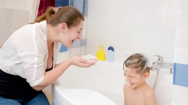 Onnellinen hymyilevä äiti ja pieni poika leikkivät saippuavaahto kylvyssä kotona. Käsitys lasten hygieniasta ja terveydenhoidosta kotona. Perhe pitää hauskaa ja pelaa — kuvapankkivideo