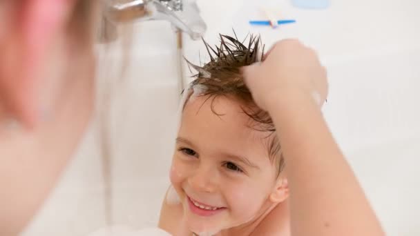 Portret wesołego uśmiechniętego chłopca z mokrymi włosami myjącego się w wannie z młodą troskliwą matką. Pojęcie higieny dzieci i opieki zdrowotnej w domu. Rodzina dobrze się bawi i gra. — Wideo stockowe