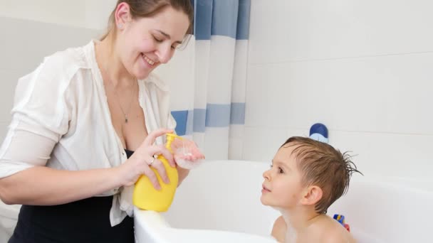 年轻有爱心的母亲微笑着，用肥皂洗洗坐在浴缸里的小男孩。家庭内儿童卫生和保健的概念。有时间在一起玩的家庭 — 图库视频影像
