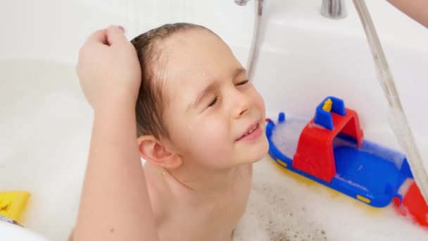 Mouvement lent du petit garçon fermant les yeux tandis que la mère se lave la tête avec un shampooing sous la douche dans le bain. Concept d'hygiène infantile et de soins de santé à domicile. — Video