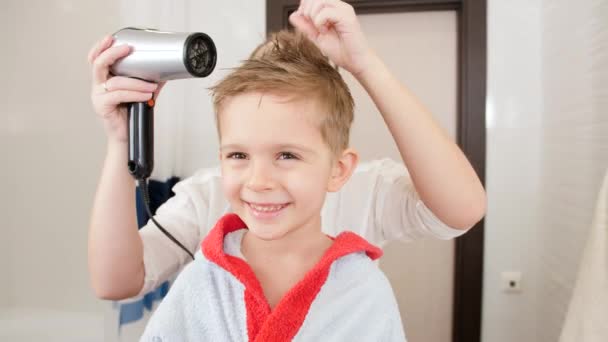 Felice bambino sorridente che guarda nello specchio riflesso nel bagno mentre la madre asciuga i capelli con l'asciugacapelli. Concetto di igiene infantile e assistenza sanitaria a casa. Genitori e figli premurosi a casa — Video Stock