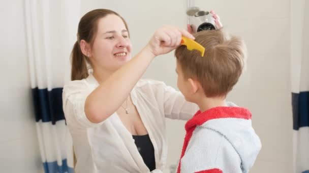 Portrét mladé matky používající fén k sušení vlasů svého malého syna po umytí v koupelně. Koncept dětské hygieny a zdravotní péče doma. Pečující rodiče a děti doma — Stock video